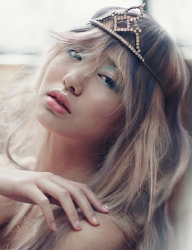 Portrait of an adult female with light blonde and purple hair wearing a jeweled crown, looking at the camera, indoors.