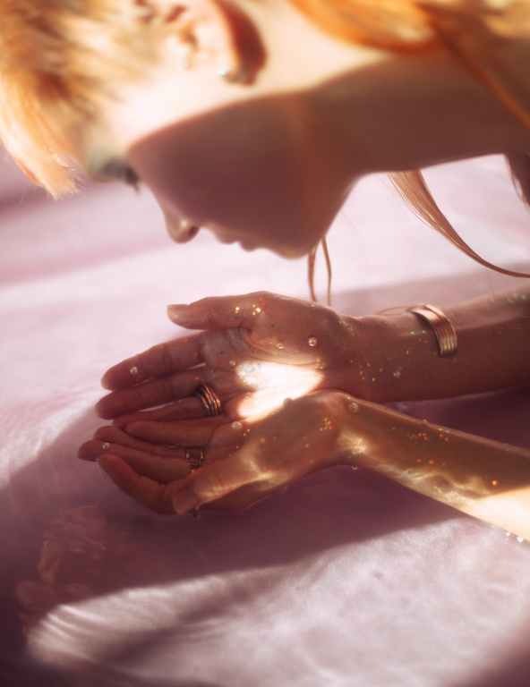 Close-up portrait of a woman cupping her hands over shimmering water with golden light reflections