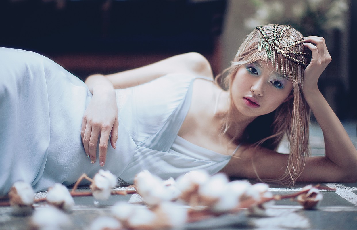 Adult female laying down in a gown with floral elements. The image is shot at eye-level with shallow depth of field and cool tones.