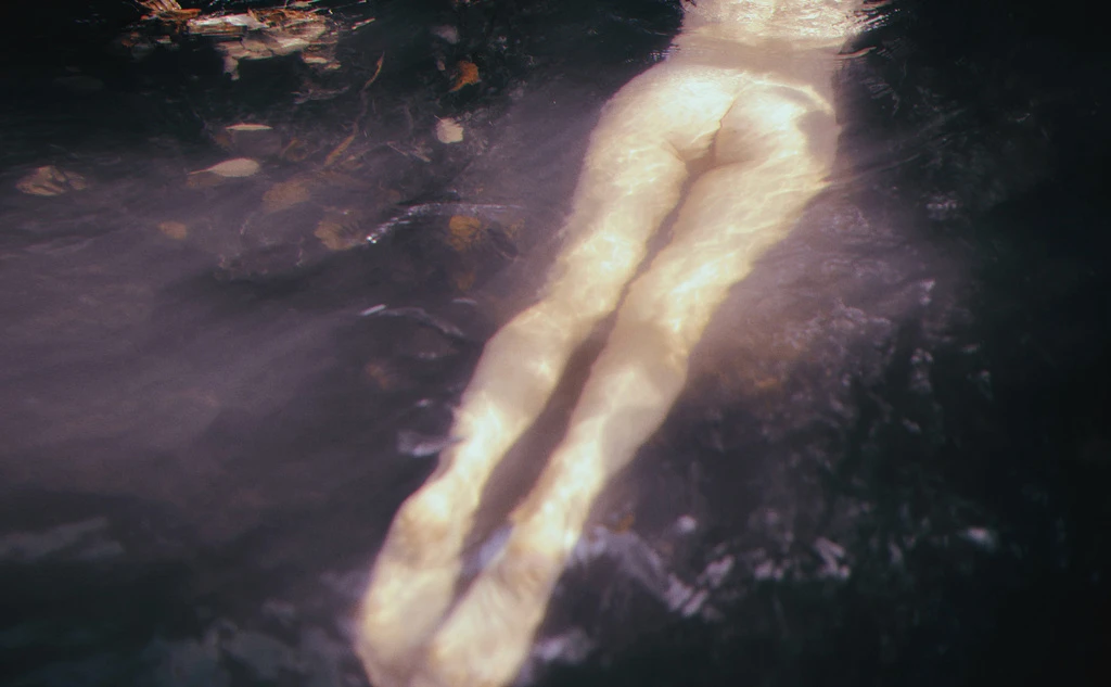 Torso and legs of a fair-skinned adult swimming in dark water, viewed from above, creating an intimate and artistic visual narrative.