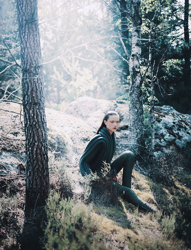 Woman in a forest wearing a green textured outfit. Sunlight filters through the trees, creating a tranquil atmosphere in nature.