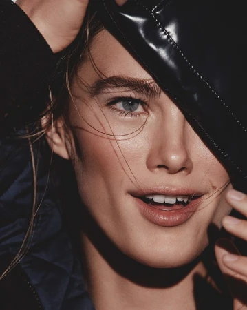Close-up portrait of a woman holding a dark shiny leather cap near her face by fashion stylist Alison Lewis.