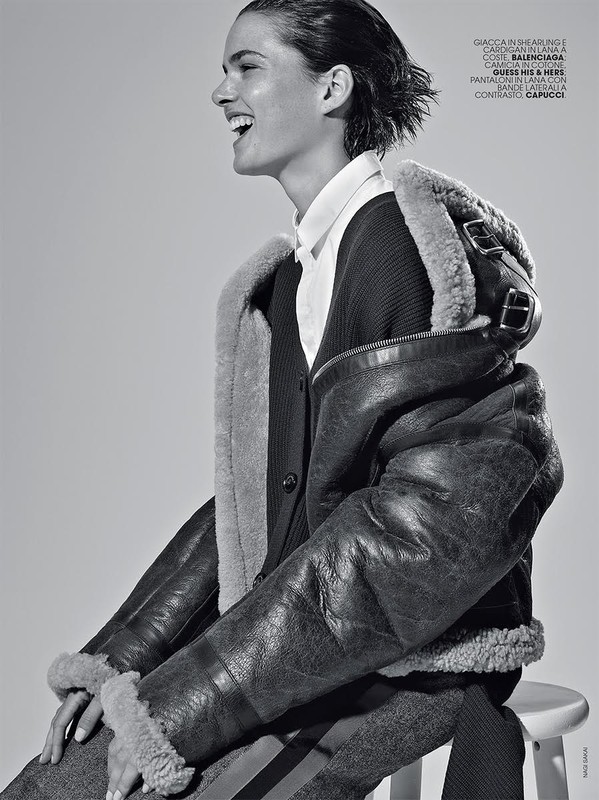 Profile view of a laughing woman wearing a shearling jacket and white collared shirt seated on a stool.