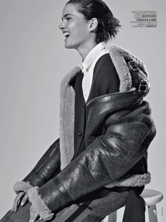 Profile view of a laughing woman wearing a shearling jacket and white collared shirt seated on a stool.