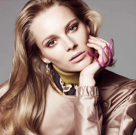 Close-up portrait of a woman with long blonde hair holding pink glasses to her chin, styled by Alison Lewis in Los Angeles.