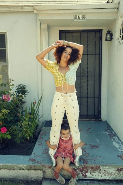 Woman and child posing on front steps of a house. The woman wears a checkered top and patterned jeans, the child wears a printed dress.