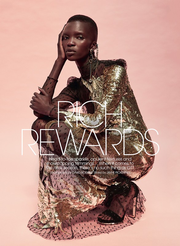 Fashion editorial shot: woman in golden sequin dress poses against a pink backdrop. Statement earrings and sheer dotted details.