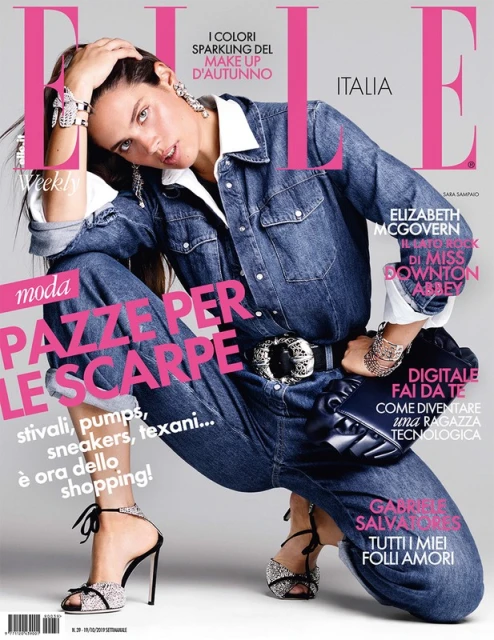 Elle Italia magazine cover featuring a posing fashion model in denim jumpsuit and embellished high-heeled sandals in a studio setting.