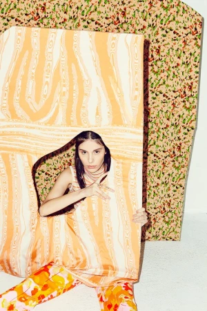 A woman poses with an orange pattern against a similar backdrop in a fashion setting, showcasing contemporary studio portrait photography.