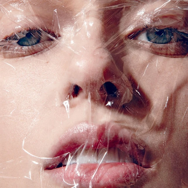 Close-up portrait of a person's face covered in clear plastic wrap, highlighting their eyes, nose, and mouth with soft, diffused lighting.