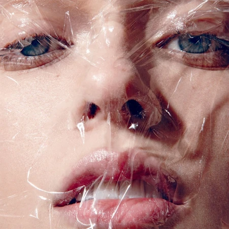 Close-up portrait of a person's face covered in clear plastic wrap, highlighting their eyes, nose, and mouth with soft, diffused lighting.