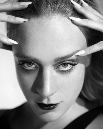 Close-up monochrome portrait of a woman with long white fingernails touching her hair, styled by Alison Lewis.