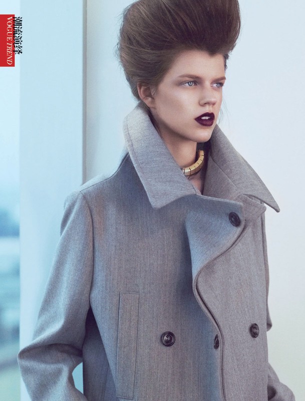 Fashion editorial portrait of a fair-skinned young adult female with dark lipstick in a grey wool coat and gold necklace in a studio.