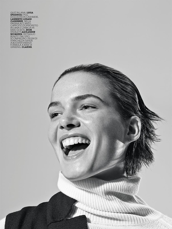 Black and white portrait of a smiling woman with wet-look hair wearing a turtleneck and vest in a studio with soft, diffused lighting.