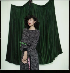 Woman in patterned black and white dress standing before a draped emerald green velvet curtain backdrop