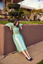 Woman in sheer mint green dress leaning against a low wall in Los Angeles by Alison Lewis