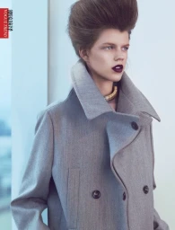 Model with high teased hair and dark lipstick wearing a grey double-breasted coat