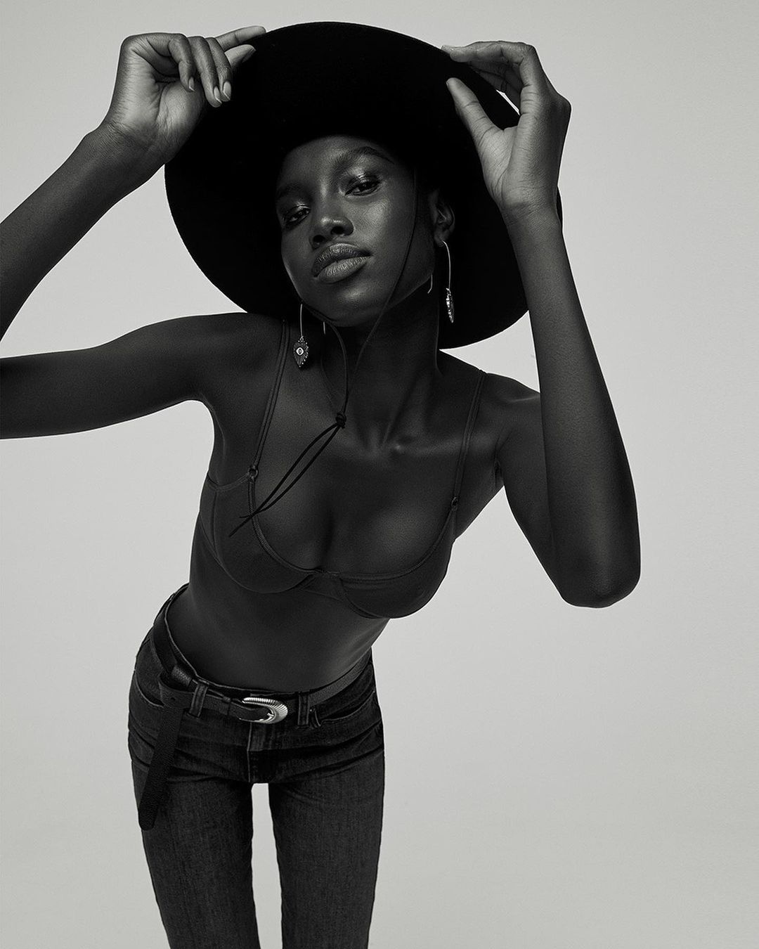 Black and white portrait of a woman wearing a wide-brimmed hat, bra top, and jeans by Amanda Pratt.