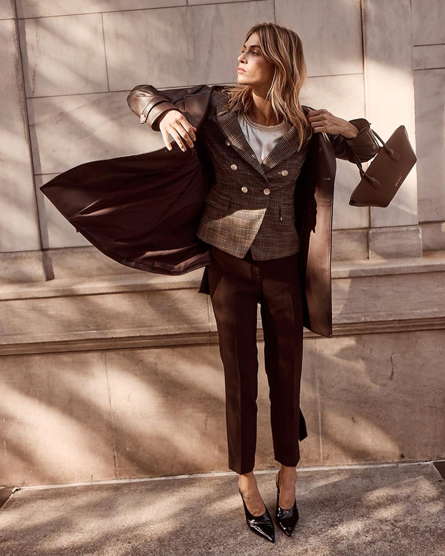 Model wearing a brown plaid blazer and dark trousers holding a handbag against a stone building exterior by photographer Amanda Pratt