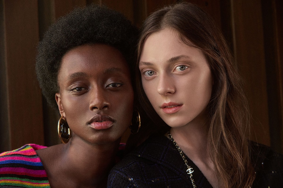 Close-up studio portrait of two young fashion models, one Black woman and one Caucasian woman, posing together in a fashion setting.