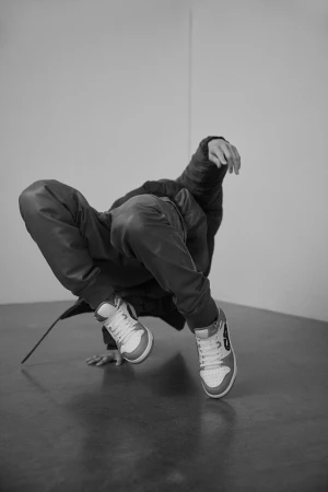 Monochrome shot of a b-boy mid-breakdance move, showcasing sneakers, and wearing a hoodie and pants against a plain background.