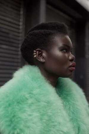 Profile portrait of a Black woman wearing a fluffy mint green faux fur coat and small ear cuffs, photographed by Amanda Pratt.