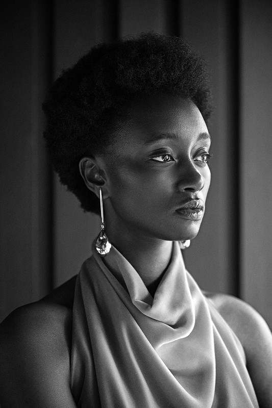 Monochrome portrait of a Black woman with an afro hairstyle wearing large, gem-like earrings and a draped light-colored garment.