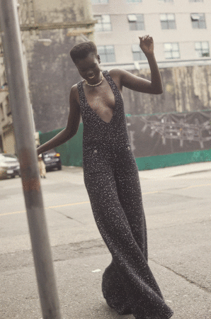 Black woman wearing a dark patterned jumpsuit walking outdoors on an urban street, photographed by Amanda Pratt