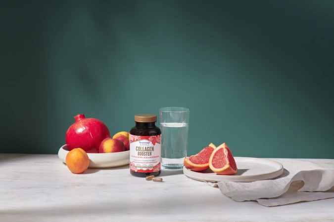 Collagen supplement bottle on a white table with fresh fruits, a glass of water, and a green background, healthy lifestyle.