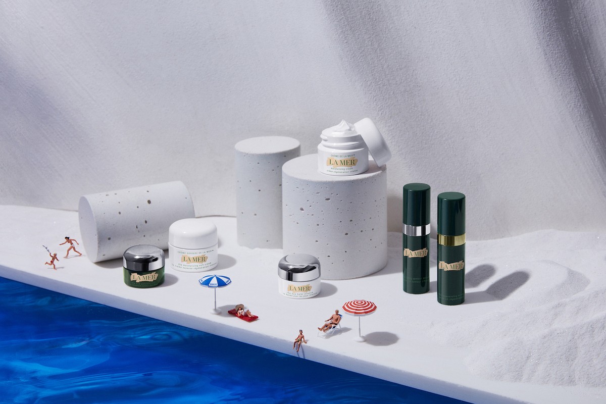 La Mer skincare product still life on a white set with blue pool and miniature people, promoting beauty and luxury.