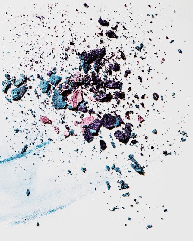 Macro studio shot of scattered blue, pink, and purple eyeshadow powder on a clean white surface, creating a colorful and textured cosmetic background.