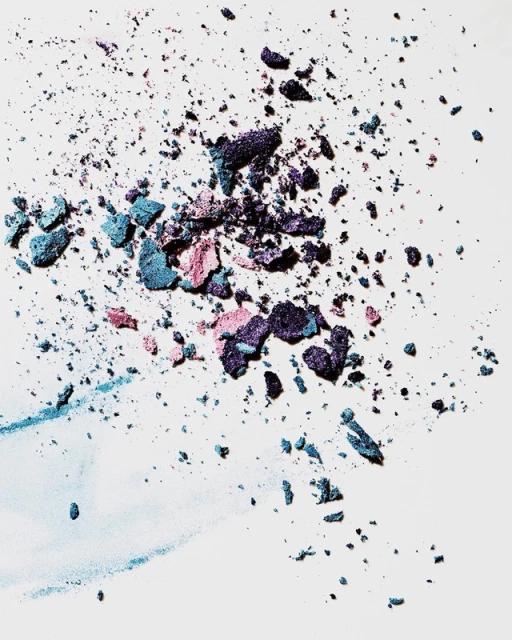 Macro studio shot of scattered blue, pink, and purple eyeshadow powder on a clean white surface, creating a colorful and textured cosmetic background.