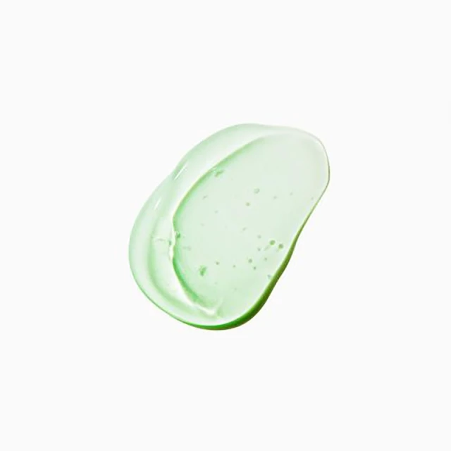 Close-up of a smear of transparent green skincare gel on a white surface, showcasing its texture and color.