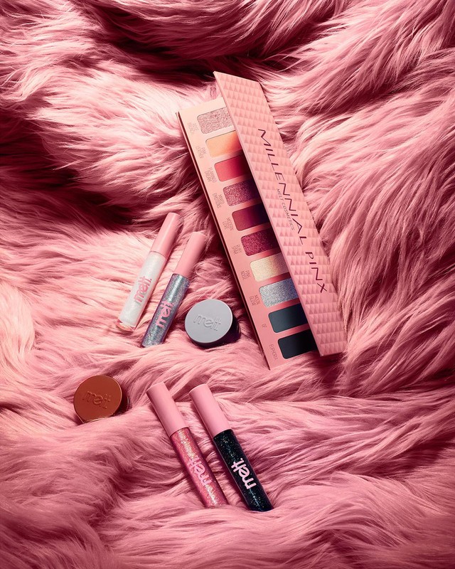 Pink-themed beauty product flat lay featuring eyeshadow palette and lip glosses on a plush faux fur background, perfect for cosmetics ads.