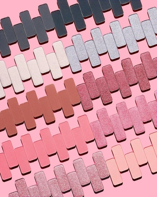Eye shadow palettes in various shades, displayed in rows on a pink background, for beauty and makeup product photography.