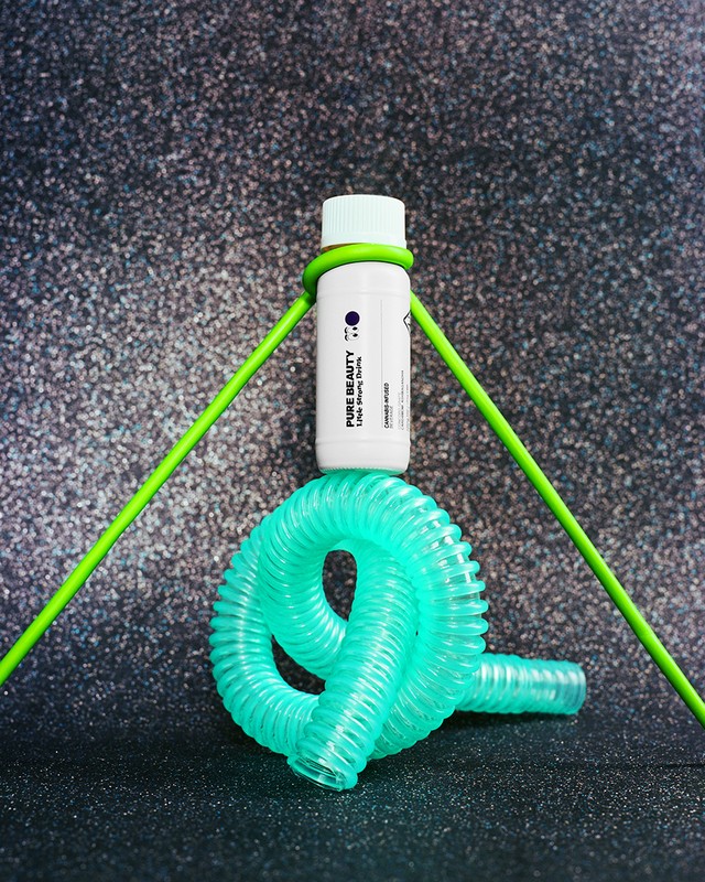 Product shot of a white bottle with green accents displayed with a green tube and blue plastic coil on a speckled background.