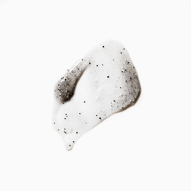 Close-up of a translucent skincare product swatch with visible black exfoliating beads against a clean, bright white background.