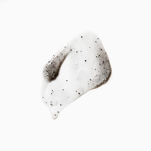 Close-up of a translucent skincare product swatch with visible black exfoliating beads against a clean, bright white background.