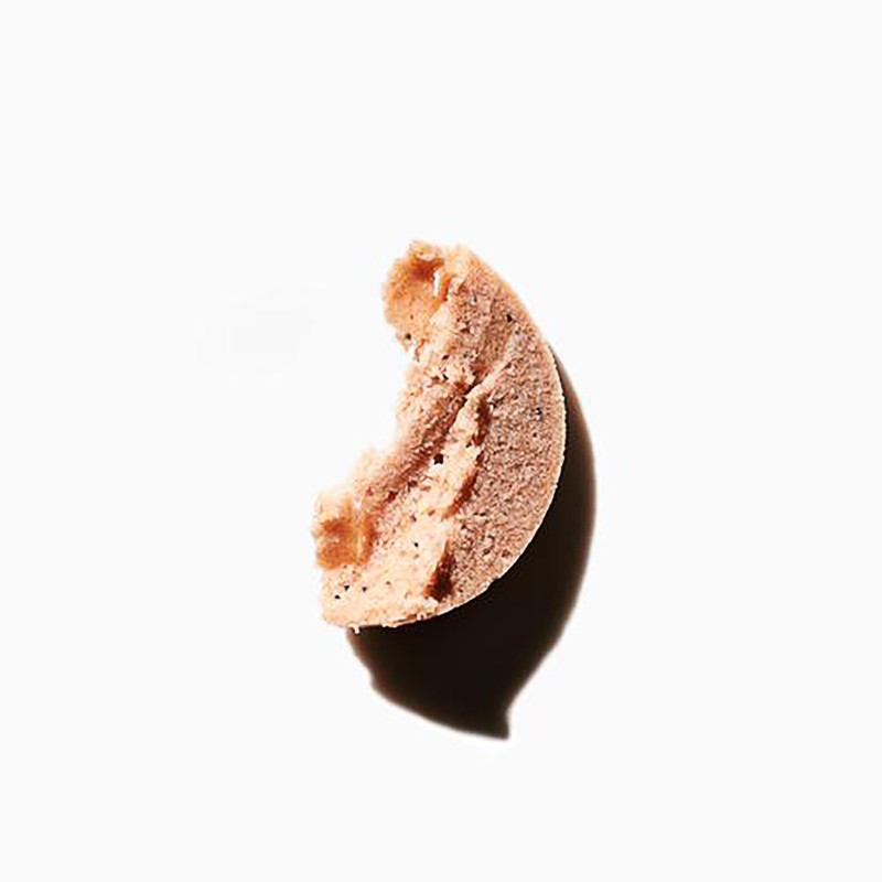 A partially eaten cookie is captured in a close-up studio shot, highlighting its crumbly texture, shadow, and the soft, neutral tones.