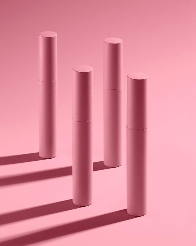 Four pink cosmetic tubes are standing on a pink background with shadows, displayed in a clean, minimalist beauty product promotional image.