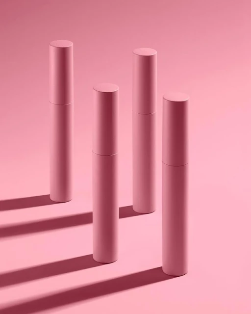 Four pink cosmetic tubes are standing on a pink background with shadows, displayed in a clean, minimalist beauty product promotional image.