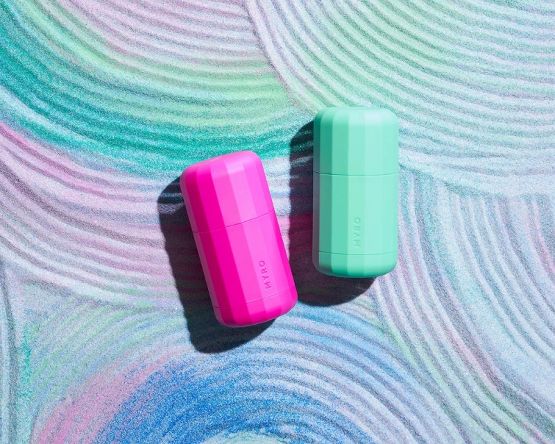 Two MYRO brand cylindrical deodorant containers, one pink and one mint green, sit on a multi-hued swirl background in a studio shot.