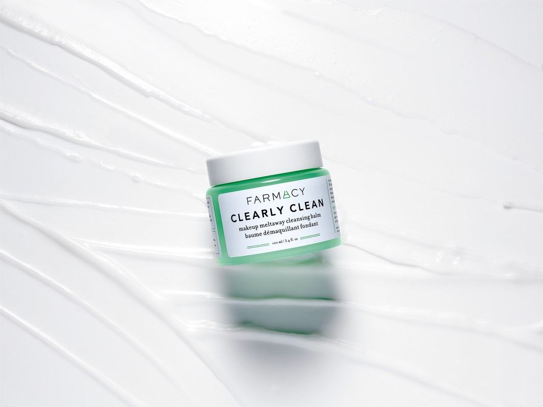 Farmacy Clearly Clean makeup remover in light green container on a white background with textured swirls, studio shot.
