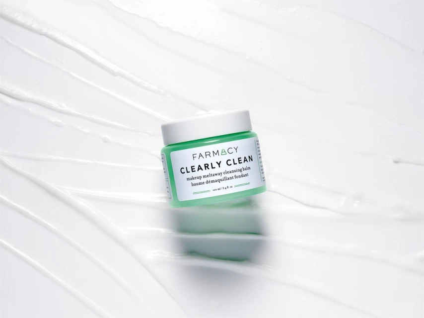 Farmacy Clearly Clean makeup remover in light green container on a white background with textured swirls, studio shot.
