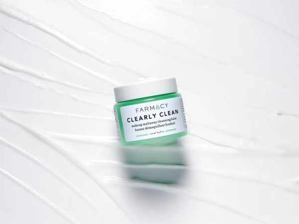Farmacy Clearly Clean makeup remover in light green container on a white background with textured swirls, studio shot.