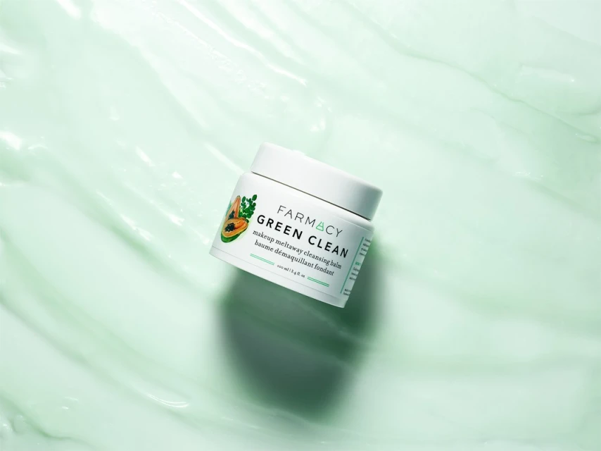 Farmacy Green Clean makeup remover balm jar on a textured light green surface. Cosmetic product photography for beauty industry.