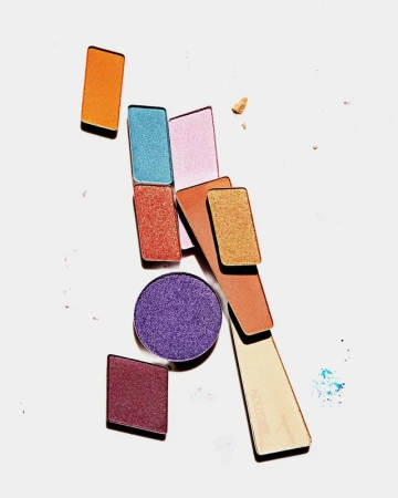 Overhead shot of arranged eyeshadow palettes in various shapes and colors, including orange, purple, and gold, on a white surface.