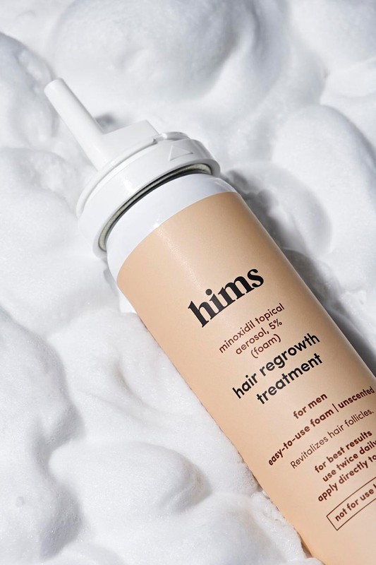 Hims brand hair regrowth treatment product on a white foamy background, close-up studio product shot, health and beauty advertisement.
