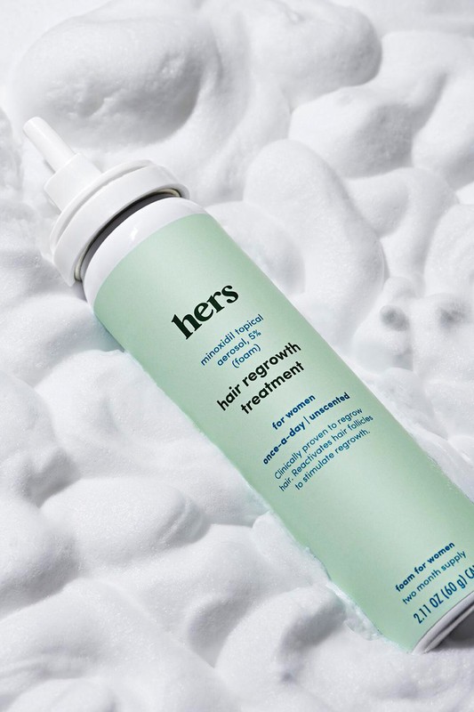 Hair regrowth treatment for women from Hers, in aerosol can, laying in a bed of white foam. Prominent branding and packaging details.