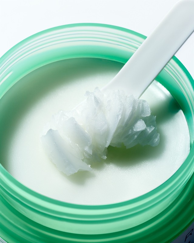 Close-up of a green jar filled with white beauty cream and a white applicator, showcasing the product's texture and consistency.